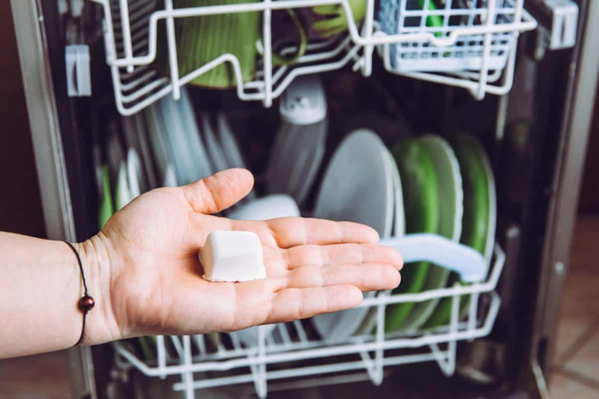 Selective focus on woman hand, holding homemade natural dishwasher pod defocus dishes in dishwasher on background