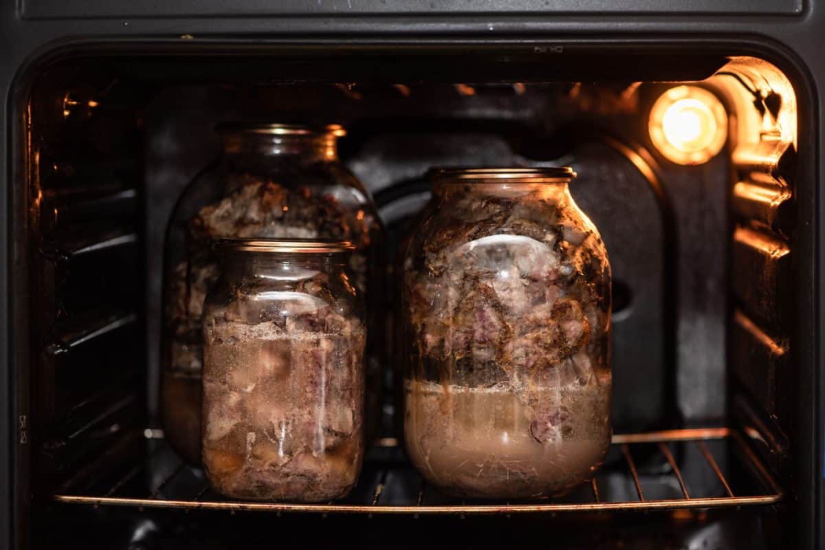 Three different sized mason jars filled with stewed pork inside an oven
