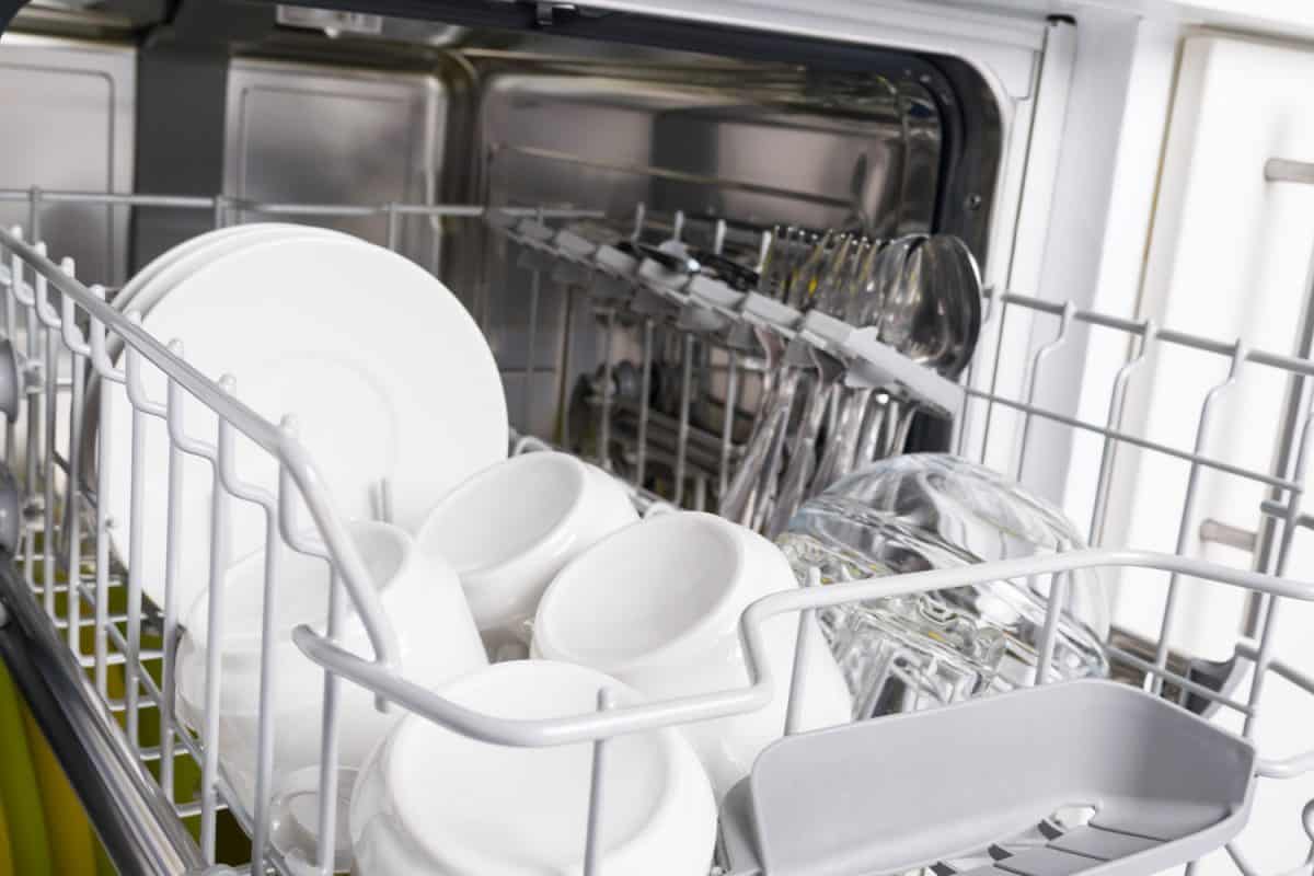 White mugs and other kitchen utensils inside the dishwasher