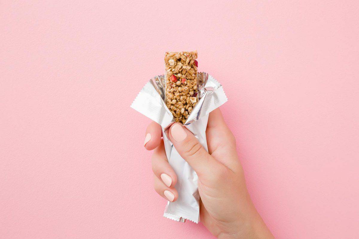 Young woman hand holding cereal bar on pastel pink table