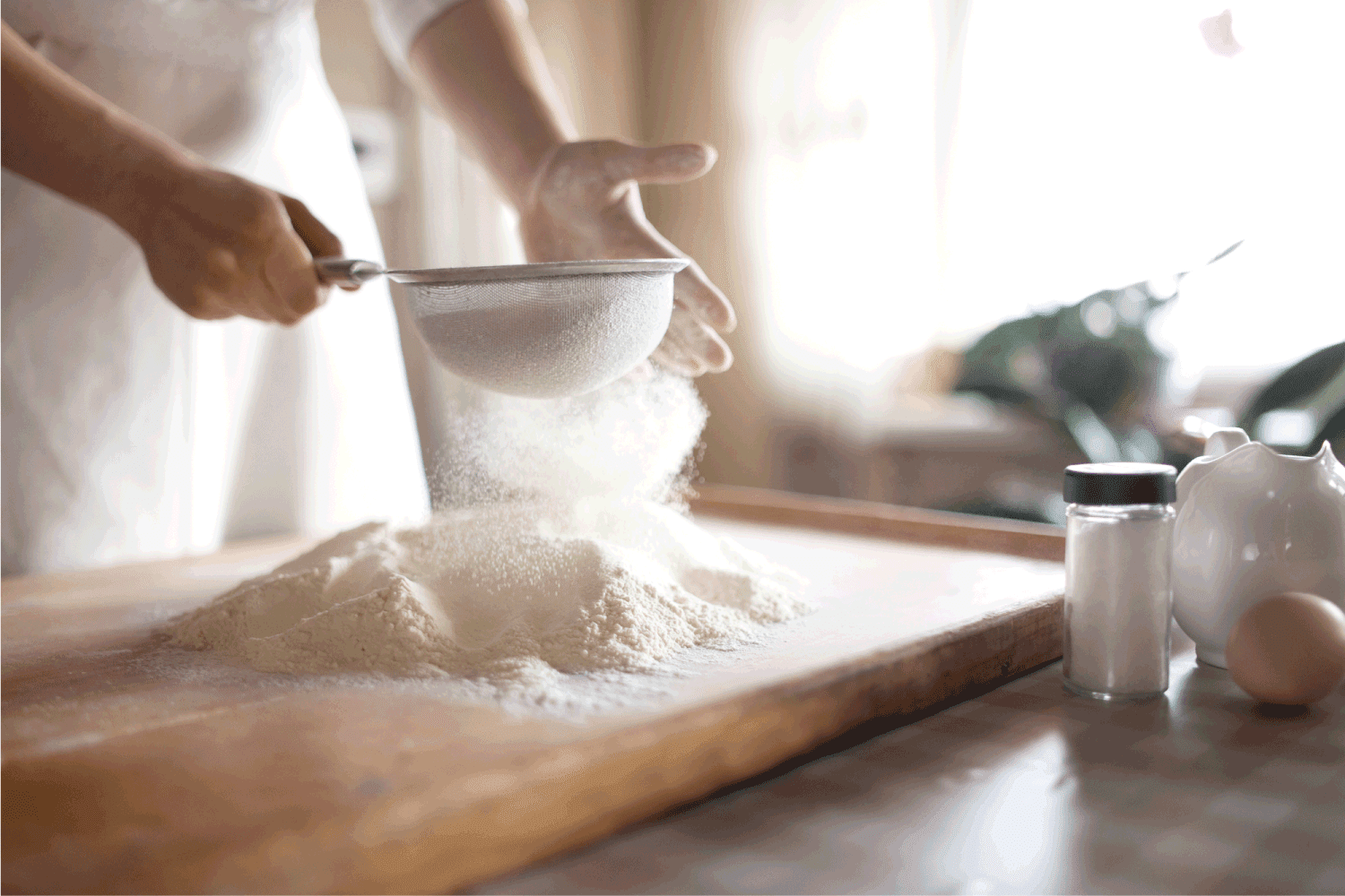 Young woman sifting flour into bowl at the kitchen