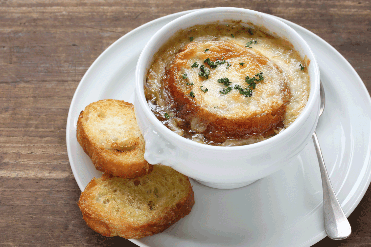french onion soup with slices of baguette on a white bowl with saucer