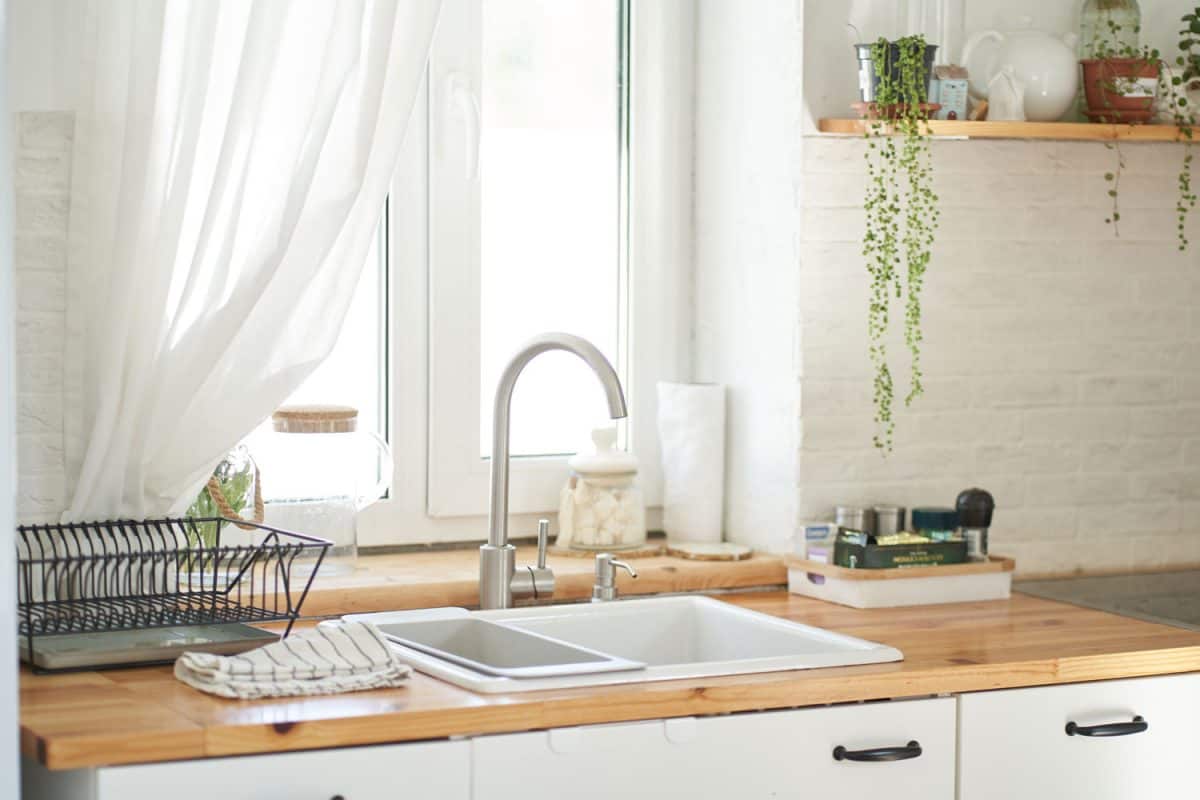 A Scandinavian themed kitchen with a wooden countertop, white minimalistic sink and a huge white framed window,