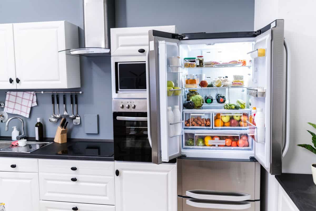 A double door fridge containing fruits, vegetables and wines placed in the corner of the kitchen