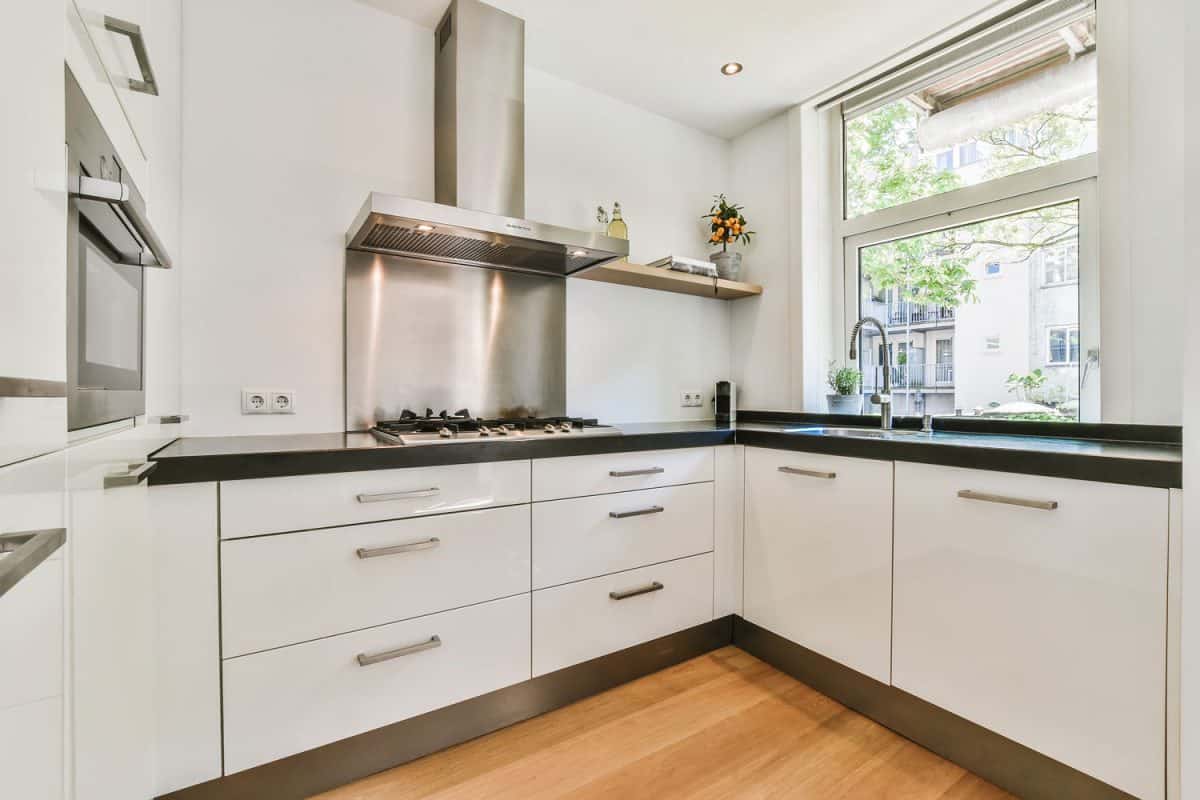 A gorgeous modern kitchen with white metal cabinets, stainless steel handles and a low kitchen window