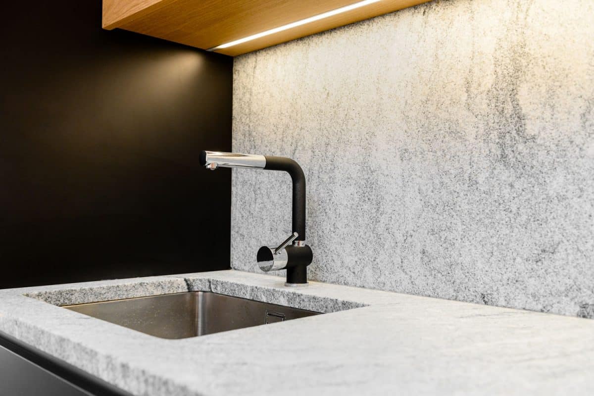 A modern and minimalist themed kitchen with stone marble countertop and black sink, Should Kitchen Sink Drain Match Faucet?