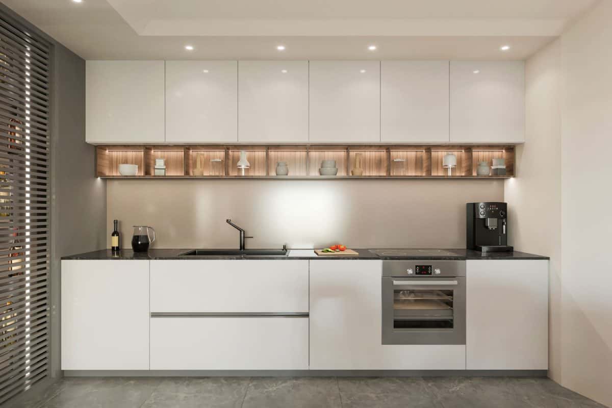 A narrow and modern kitchen area with white glass cupboards and whit cabinets and gray flooring