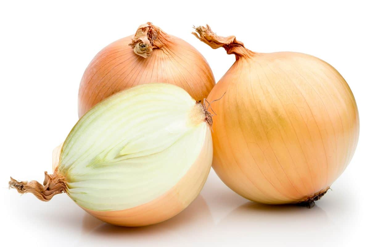 A sliced and un-peeled onion on a white background