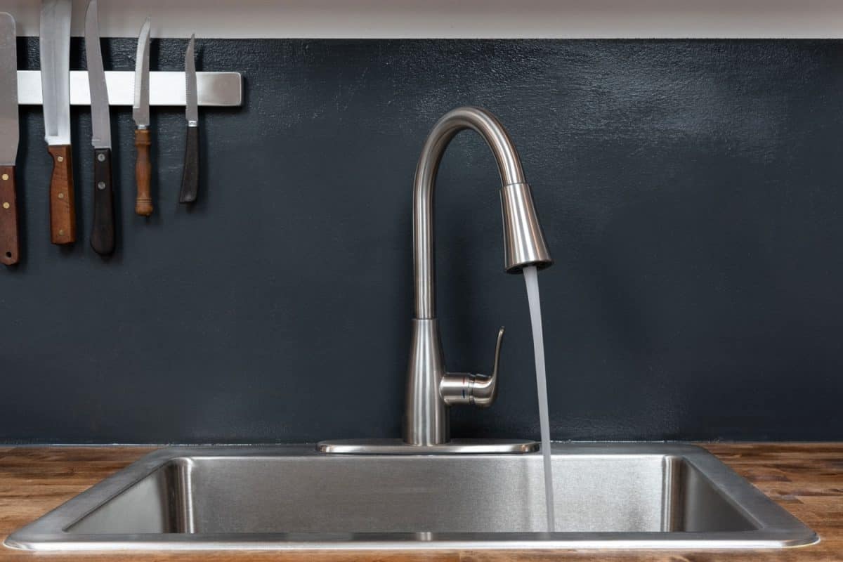 A stainless steel kitchen faucet and kitchen sink with wooden countertop