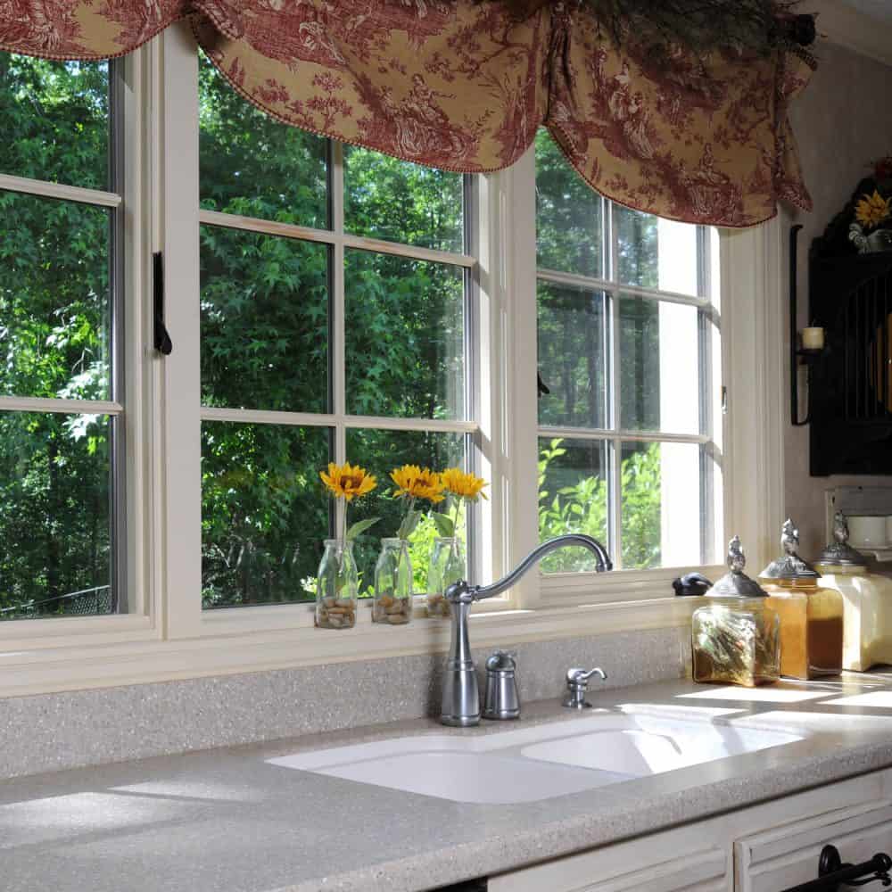 A white framed kitchen window with floral designed curtains decorated with sunflowers