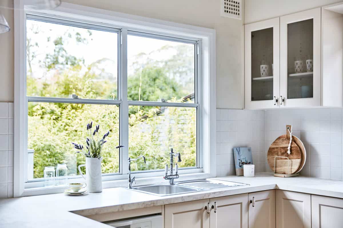A white modern kitchen with cream painted cabinets and a low kitchen window