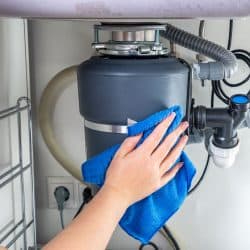 A woman cleaning the garbage disposal sink using a blue cloth, What Happens If You Leave A Garbage Disposal On?
