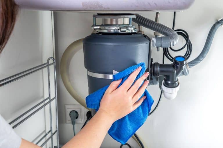 A woman cleaning the garbage disposal sink using a blue cloth, What Happens If You Leave A Garbage Disposal On?