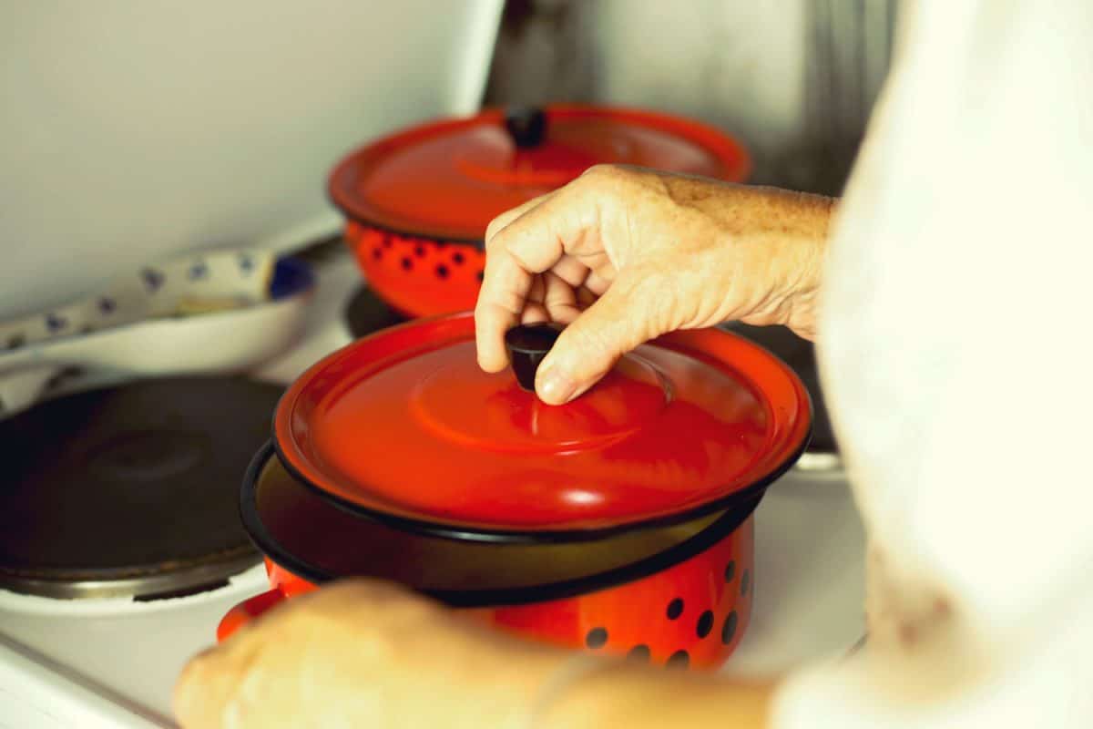 A woman opening a red enamel Dutch oven at the cooktop