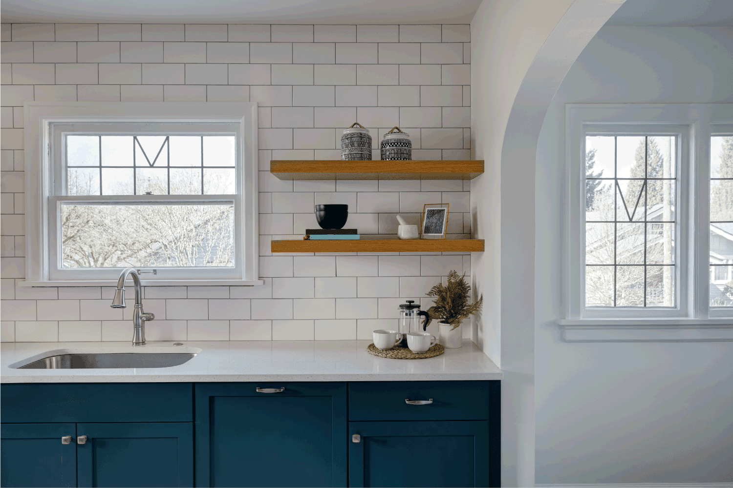 An elegant minimalist styled kitchen with white subway tiles, a window to look out and white countertops filed with decoration