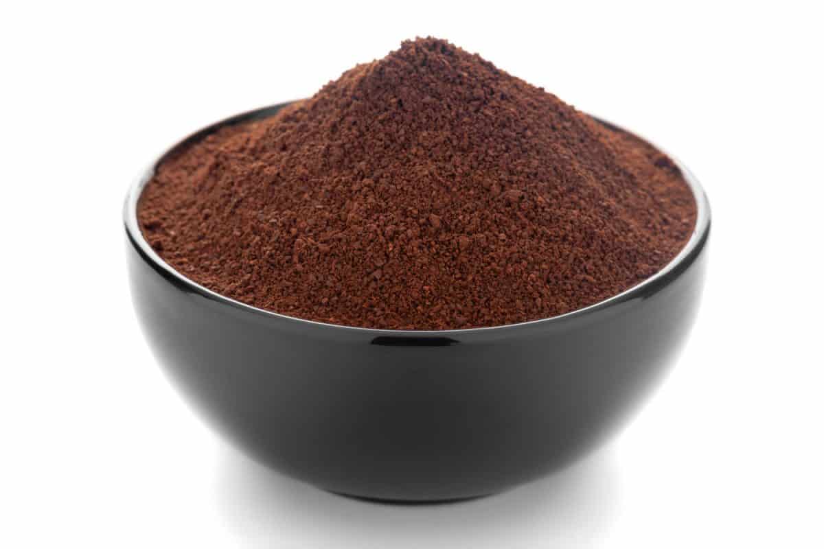 Close-Up of organic dark brown coffee granules in black ceramic bowl over white background