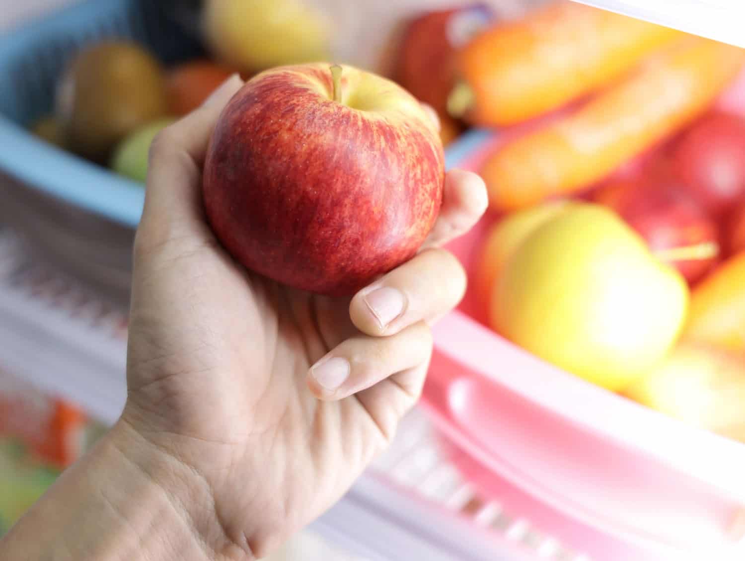 Close up of woman hand taking red apple out of refrigerator in kitchen