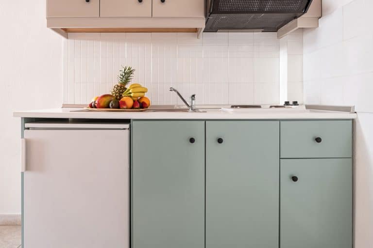 Closeup of white tile splashback on empty wall in simple cabinet module of modern interior kitchen with small fridge, vent, sink, stove, fruit plate, How To Reverse The Door On Danby Refrigerator