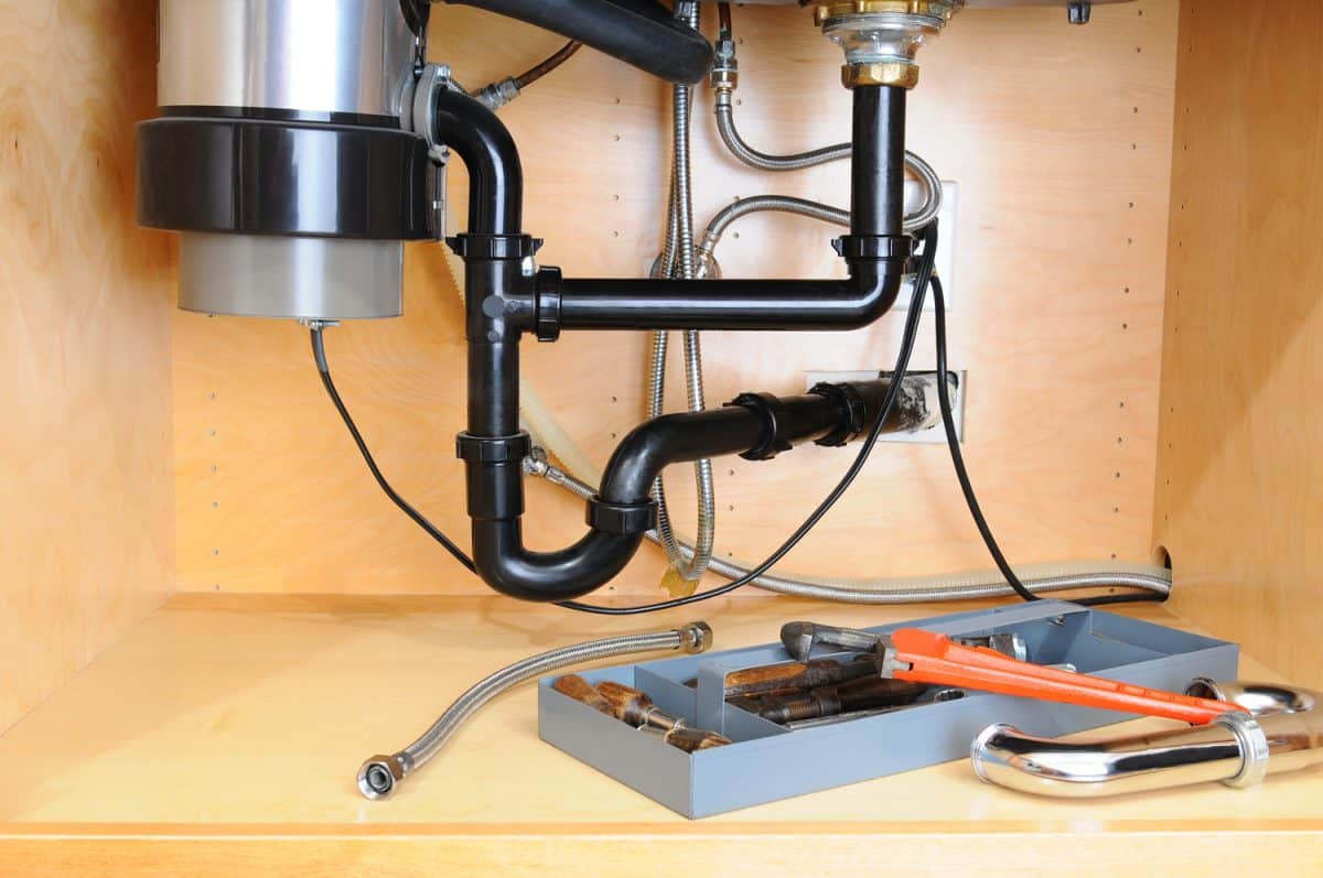 Detail of the plumbing system under a modern kitchen sink, with a plumbers tool tray and equipment.