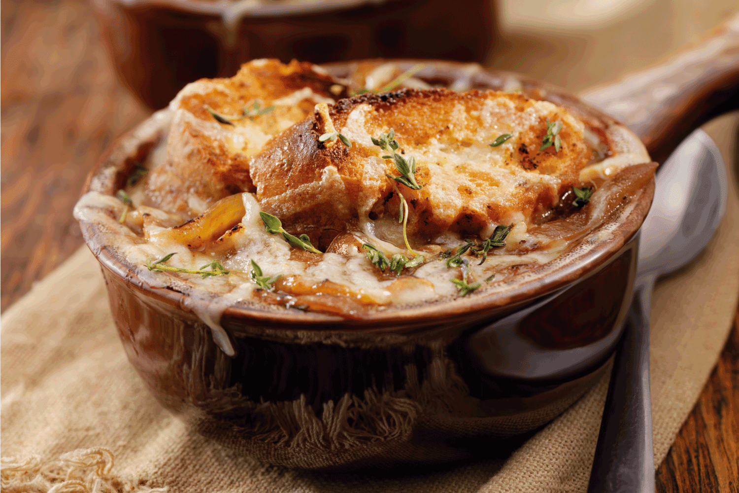 French Onion Soup on a ceramic bowl, jute placemat and metal spoon on wooden table