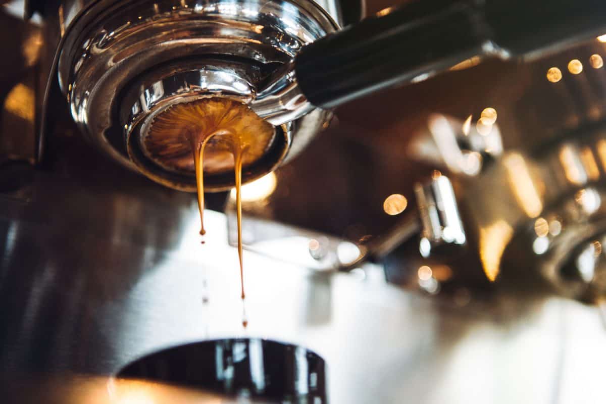 Fresh and hot espresso coffee pours from a portafilter on a nice chrome espresso machine.