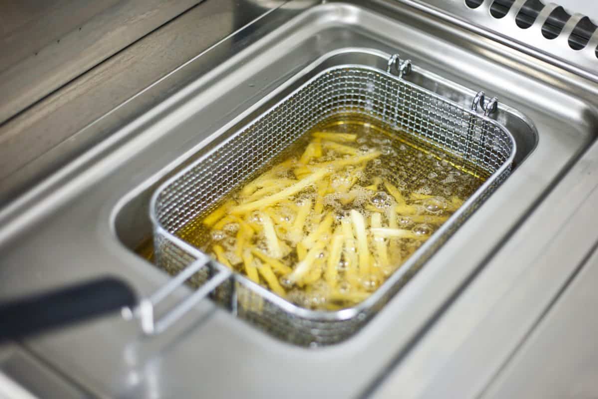 Frying French fries in cooking oil in a deep-fryer in kitchen