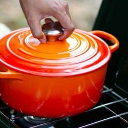 A hand putting cover on a red enameled cast iron dutch oven on camping stove, How Heavy Is A Dutch Oven?