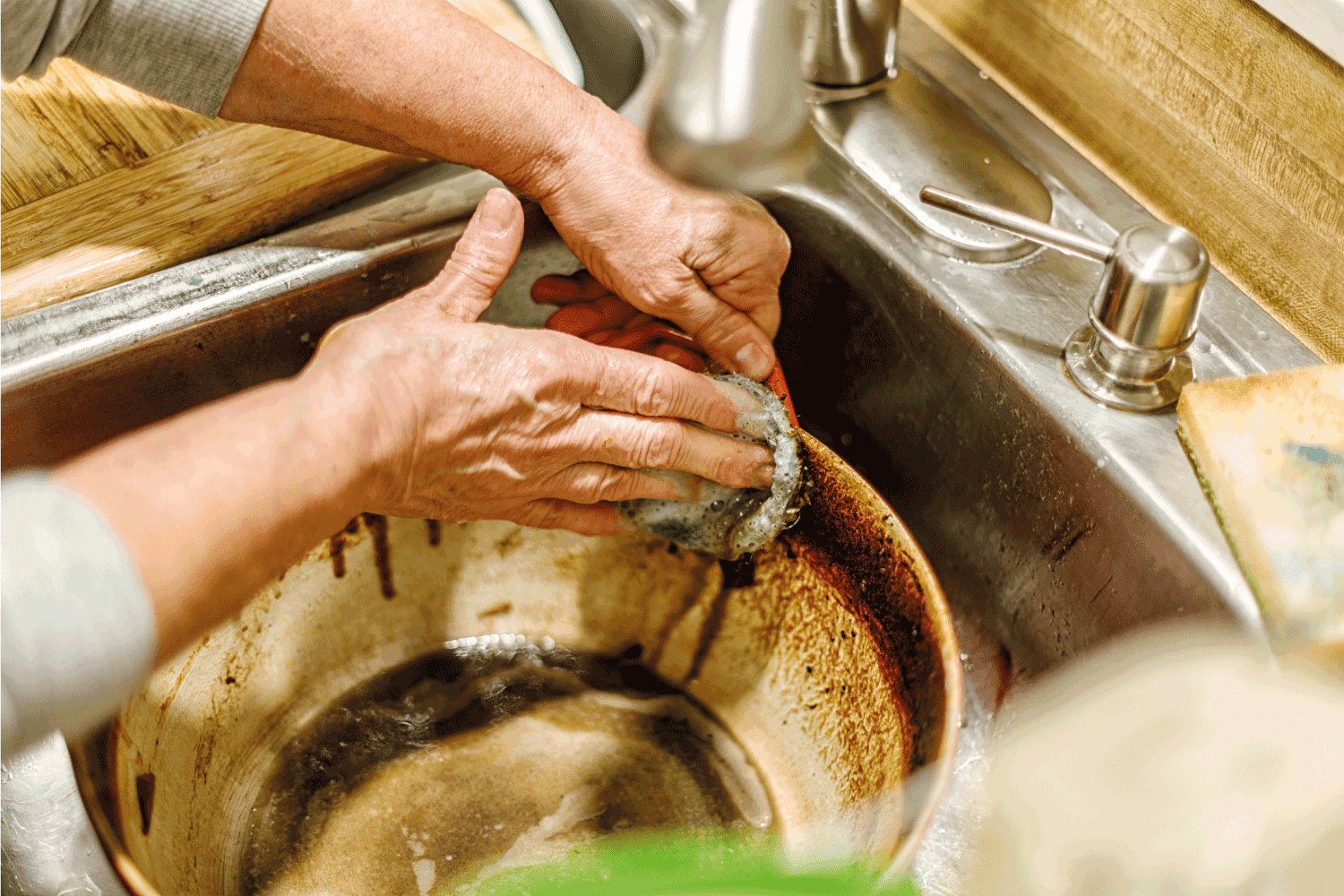 Hand washing a grimy, oily, sloppy Dutch oven cooking pan. A scouring pad is required to remove the burnt, baked-on Italian tomato sauce food residue