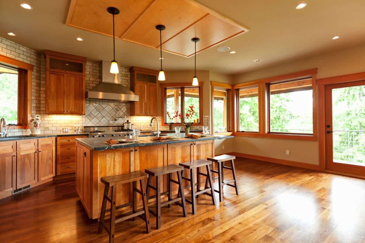Interior of a rustic themed kitchen with wooden flooring, wooden breakfast bar and huge wooden framed windows