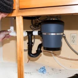 Man installing garbage disposal in home, What Happens If Glass Gets In The Garbage Disposal?