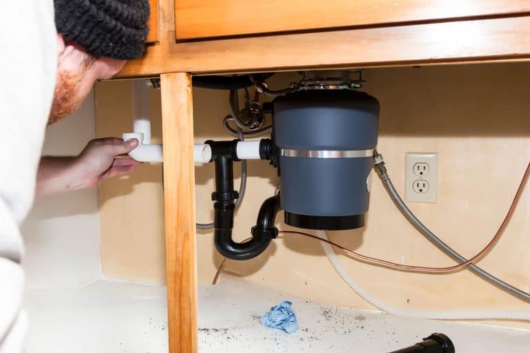 Man installing garbage disposal in home, What Happens If Glass Gets In The Garbage Disposal?