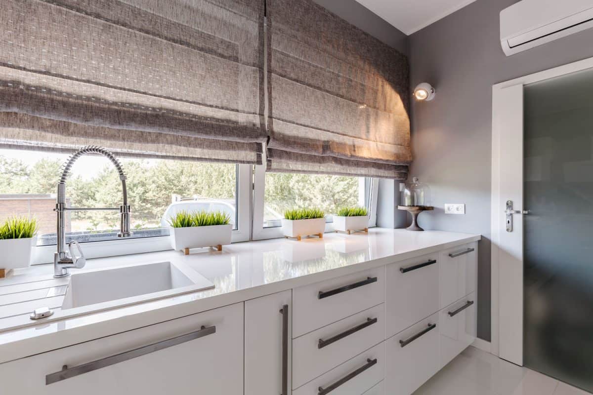 Modern inspired kitchen with stainless steel long handle cabinet and small plants near the window with blinds