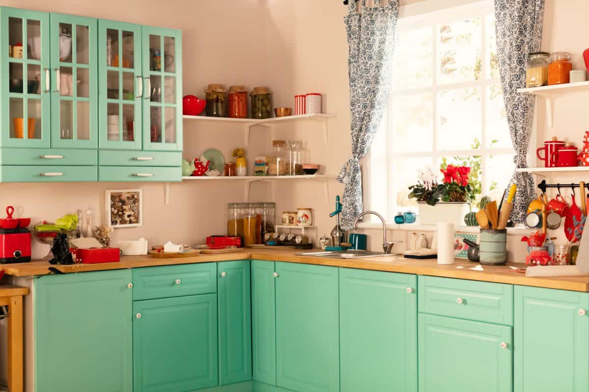 Retro inspired kitchen with a black and white curtains in the window and cyan colored kitchen cabinets