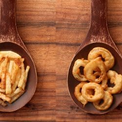 Top view of wooden spoon over wood surface with homemade onion rings and french fries on it, Onion Rings Vs French Fries: Which To Choose?