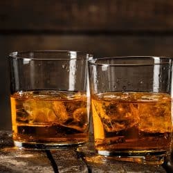 Two glasses whiskey with ice cubes on wooden background, How Often Should You Replace Drinking Glasses?
