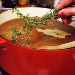 Woman placing sprig of thyme in a pot of French onion soup, How Many Quarts In A Dutch Oven?