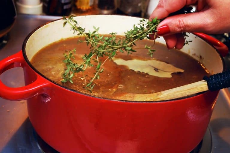 Woman placing sprig of thyme in a pot of French onion soup, How Many Quarts In A Dutch Oven?