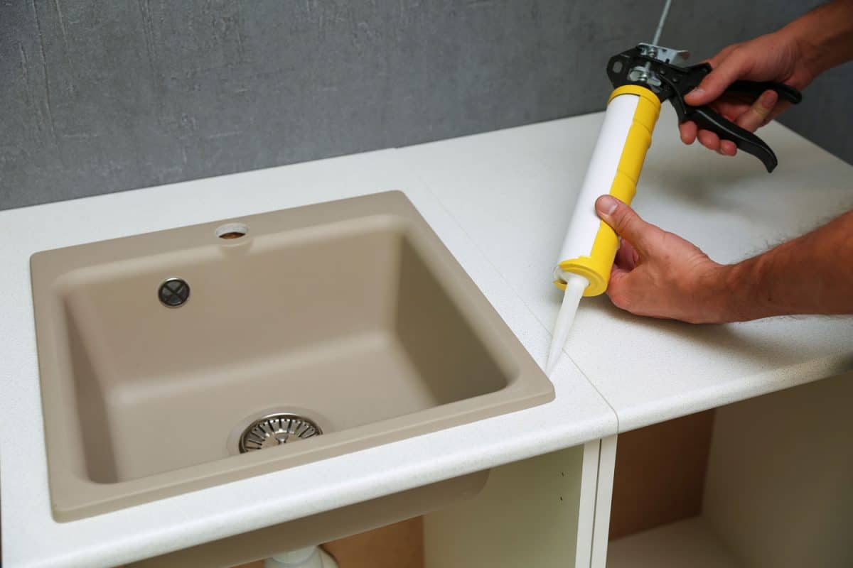worker seals kitchen sink with sealant