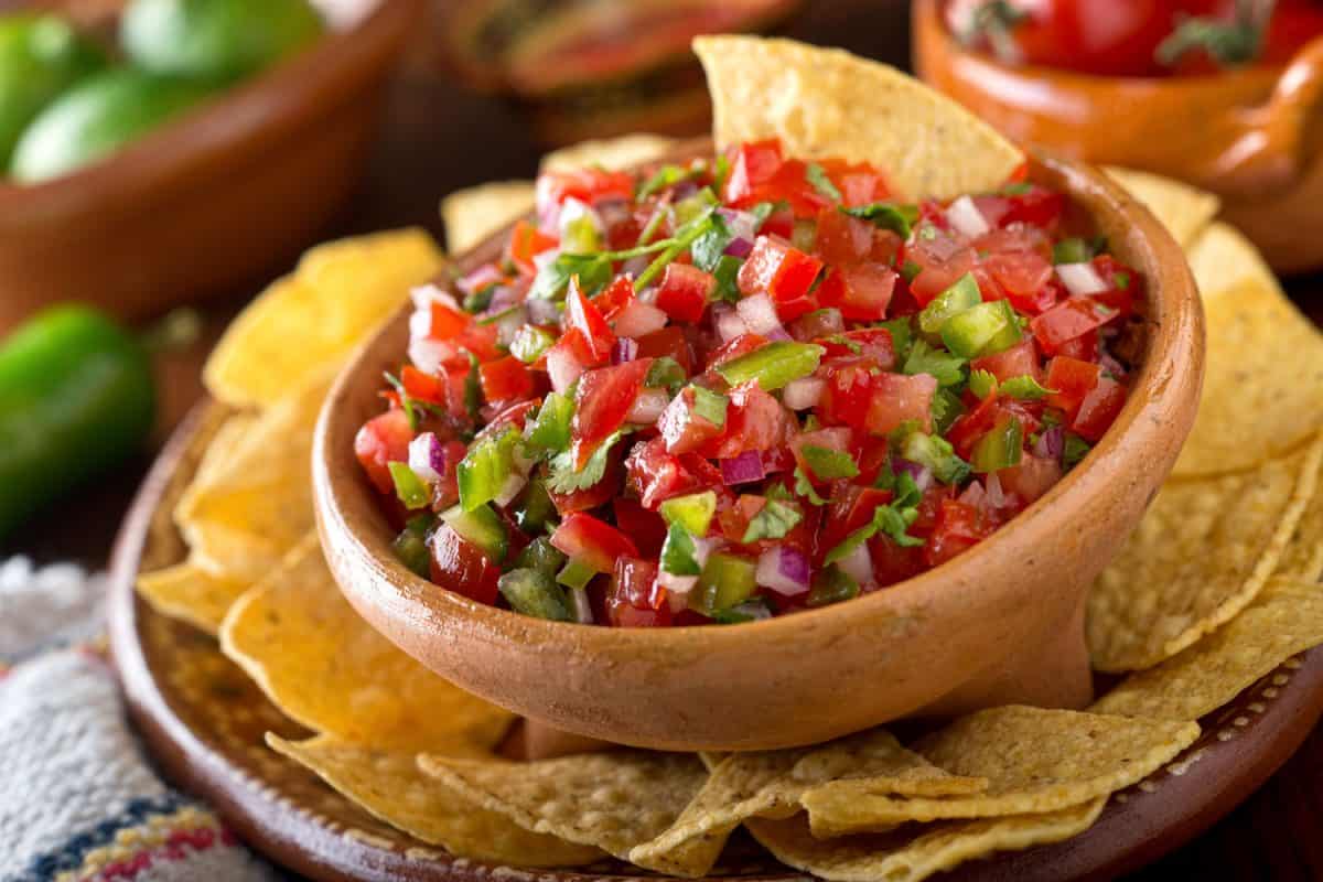 A bowl of Pico de Gallo with tortilla chips on the sides served with citrus