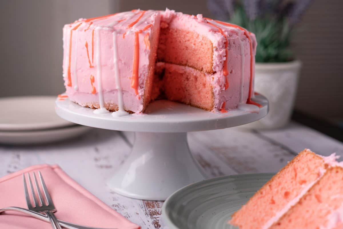 A pink buttercream frosted cake with red and white glaze dripping down the sides