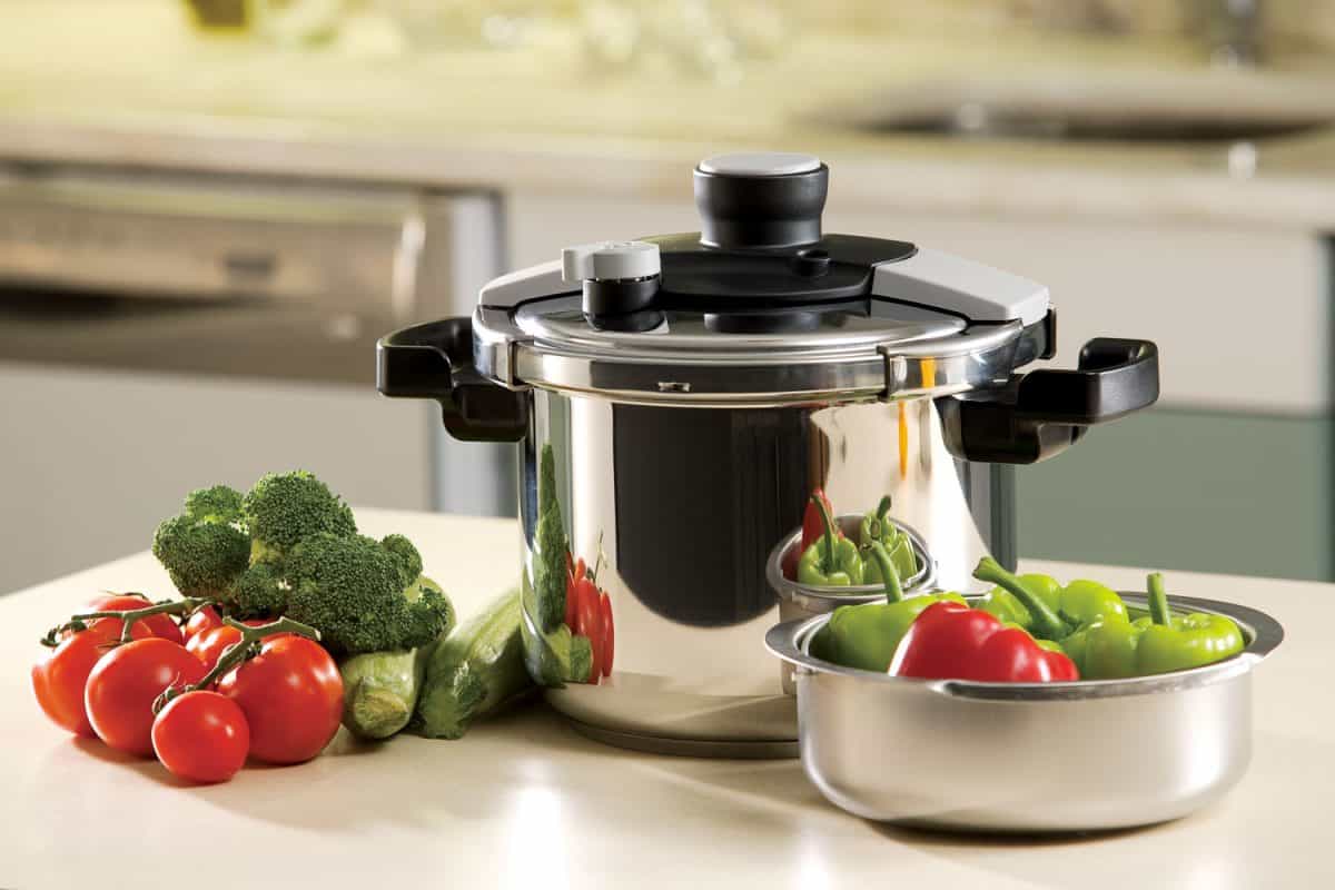 A pressure cooker on the center island countertop with veggies on the sides