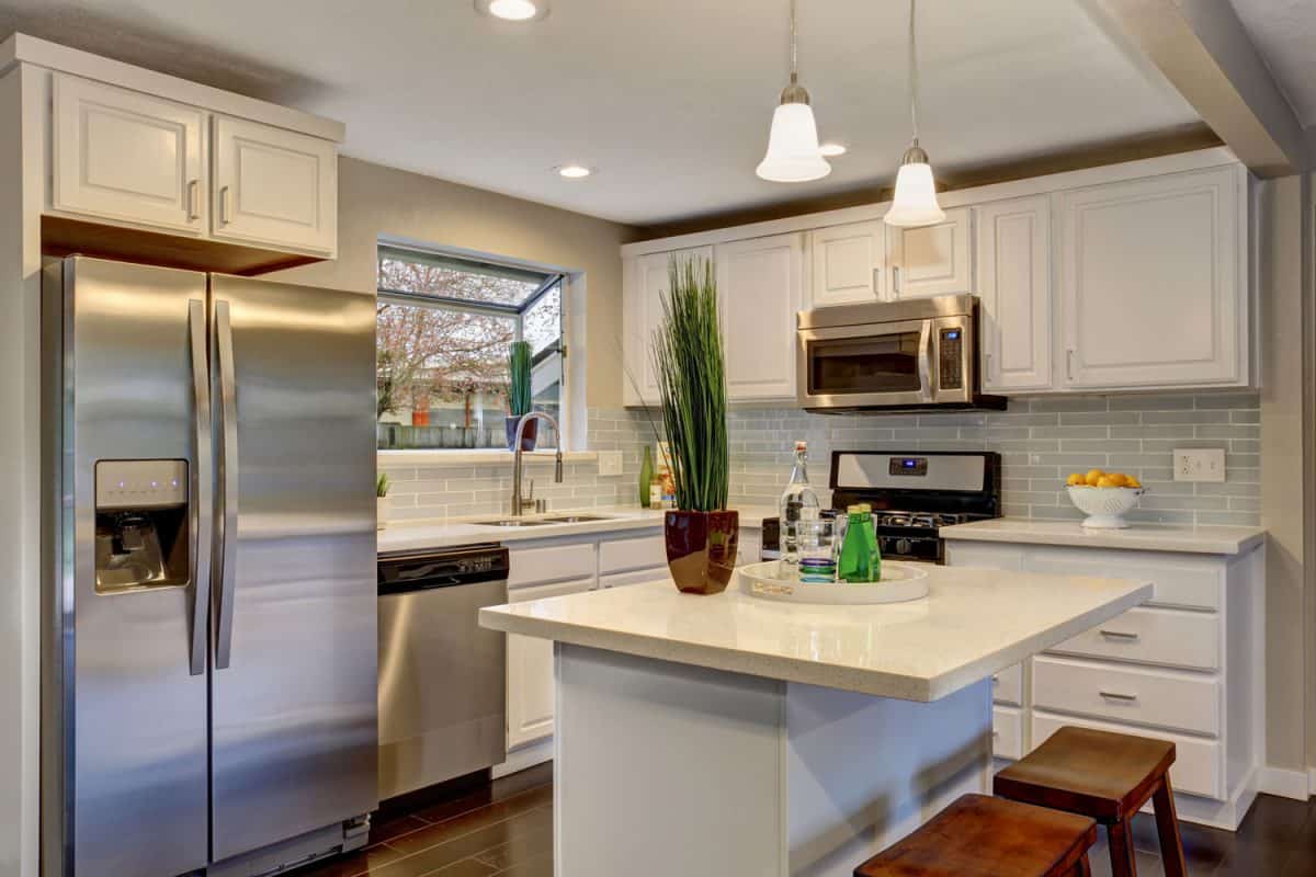 A spacious kitchen with a breakfast bar dangling lamps and a refrigerator on the corner