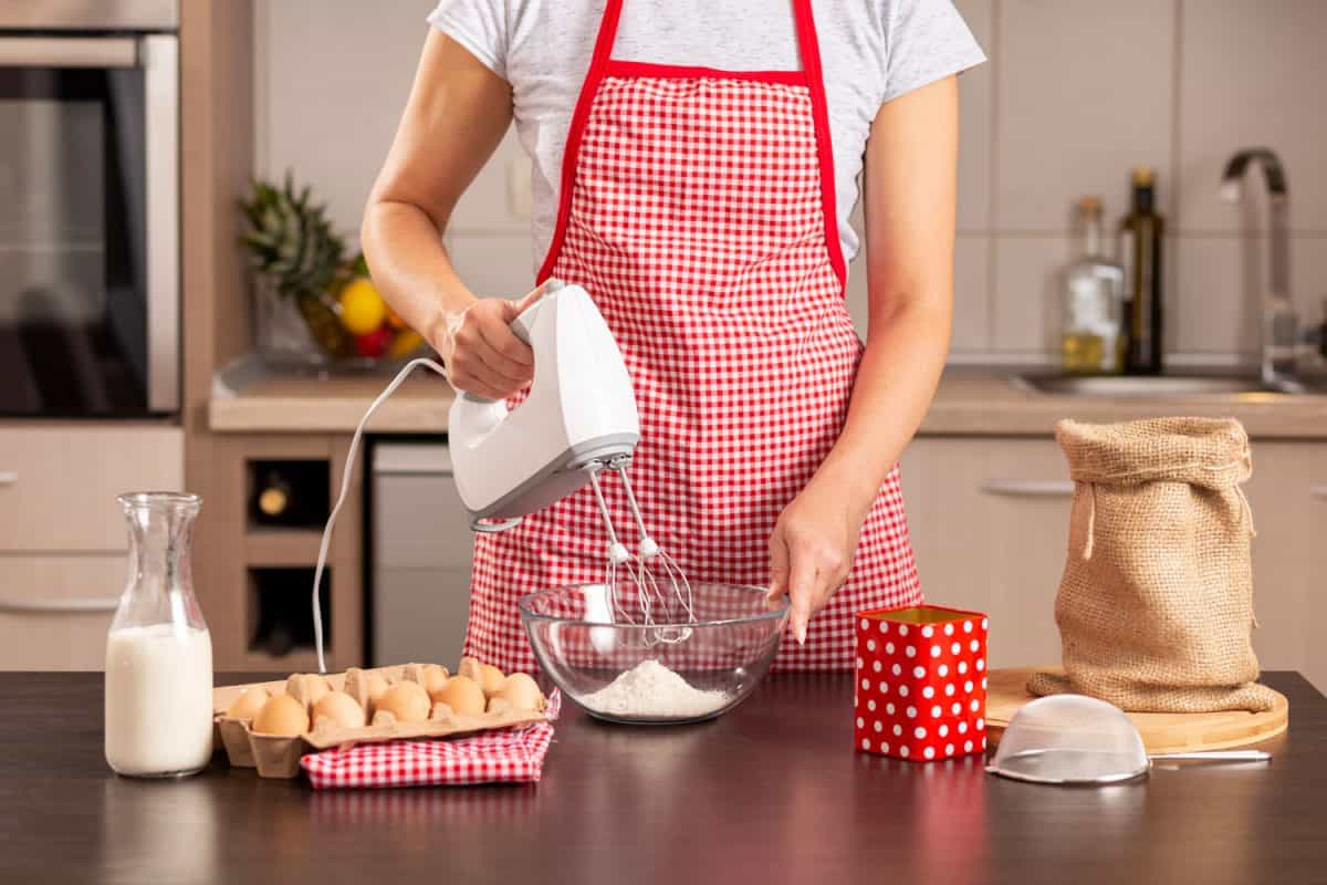 A tall woman wearing a polka dotted apron and holding a white hand mixer