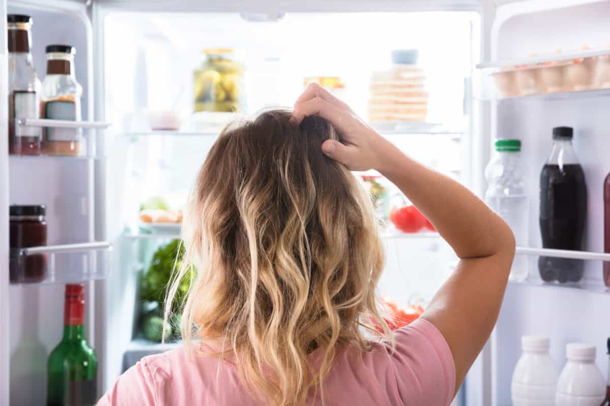 A woman scratching her head because fridge is full