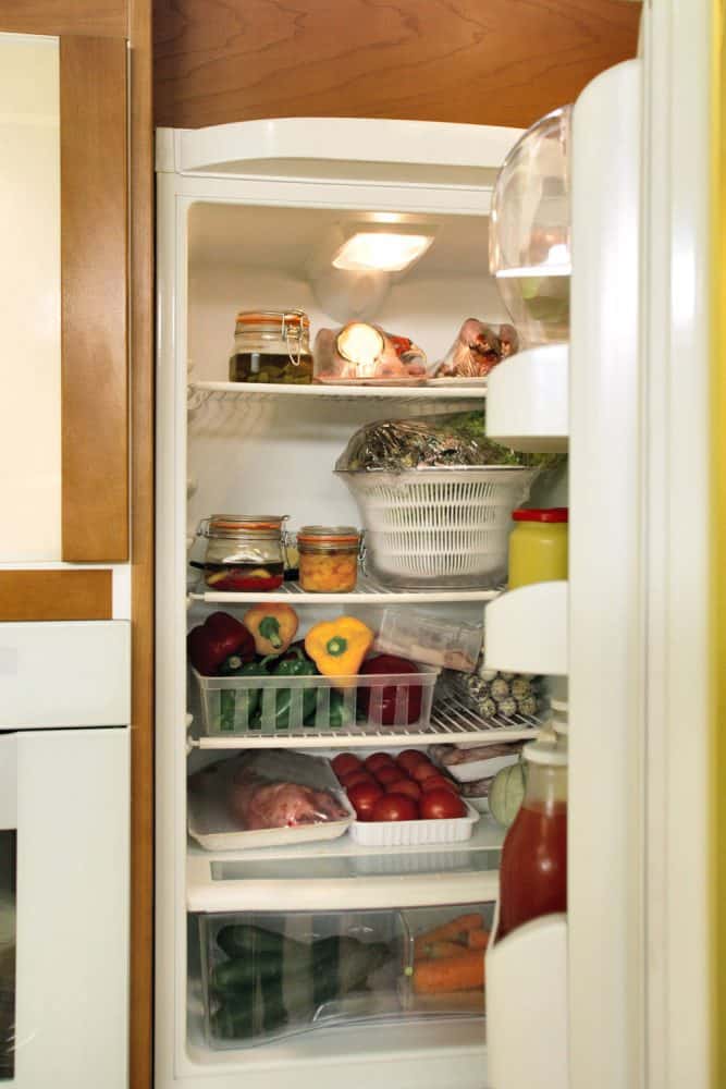 An opened fridge containing lots of vegetables and fruits
