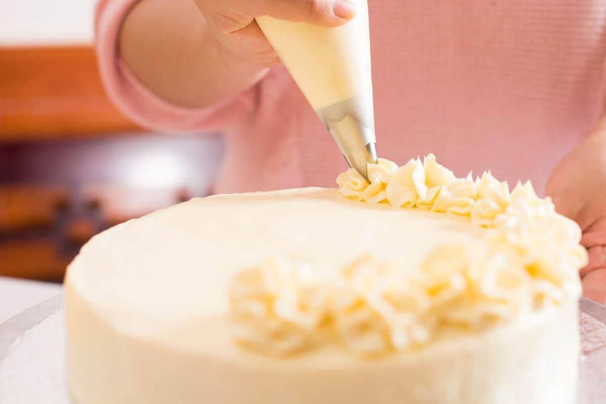 Close shot of a human hand frosting a cake with whipped cream on the foreground
