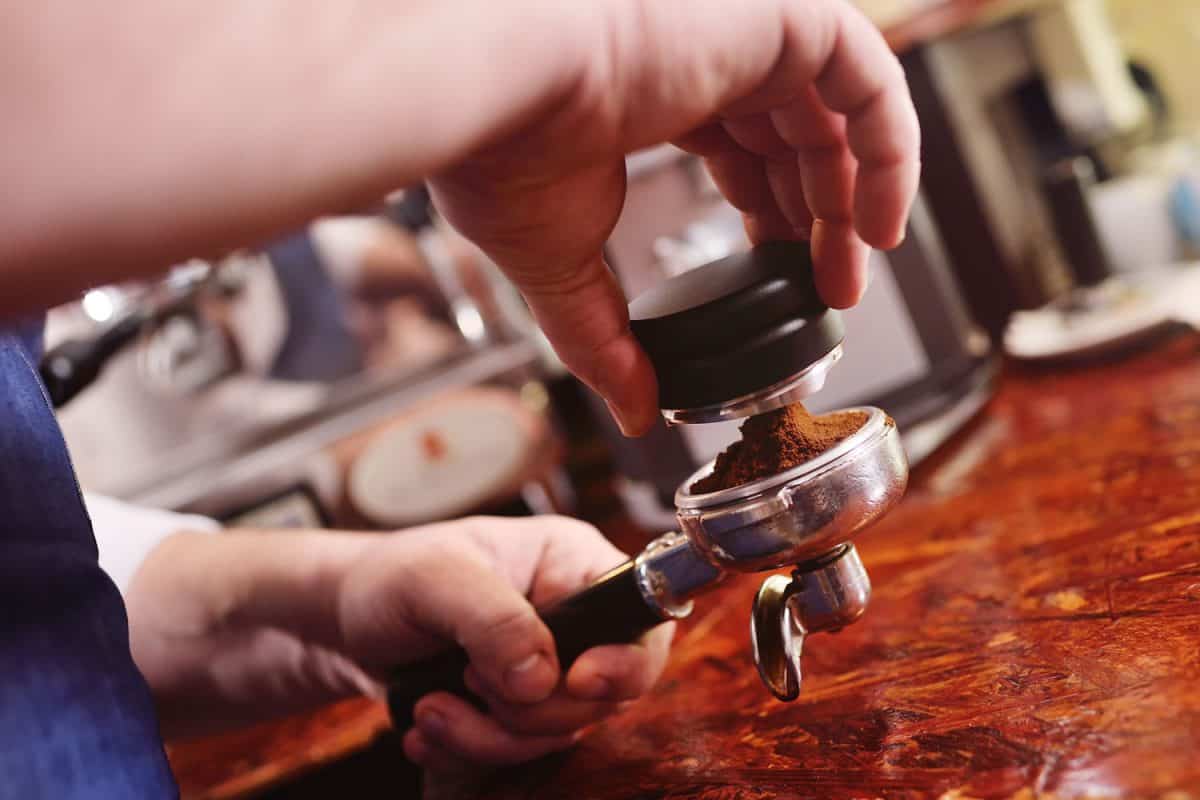 Holder with ground coffee and tamper for forming coffee pill close-up in the hands of barista