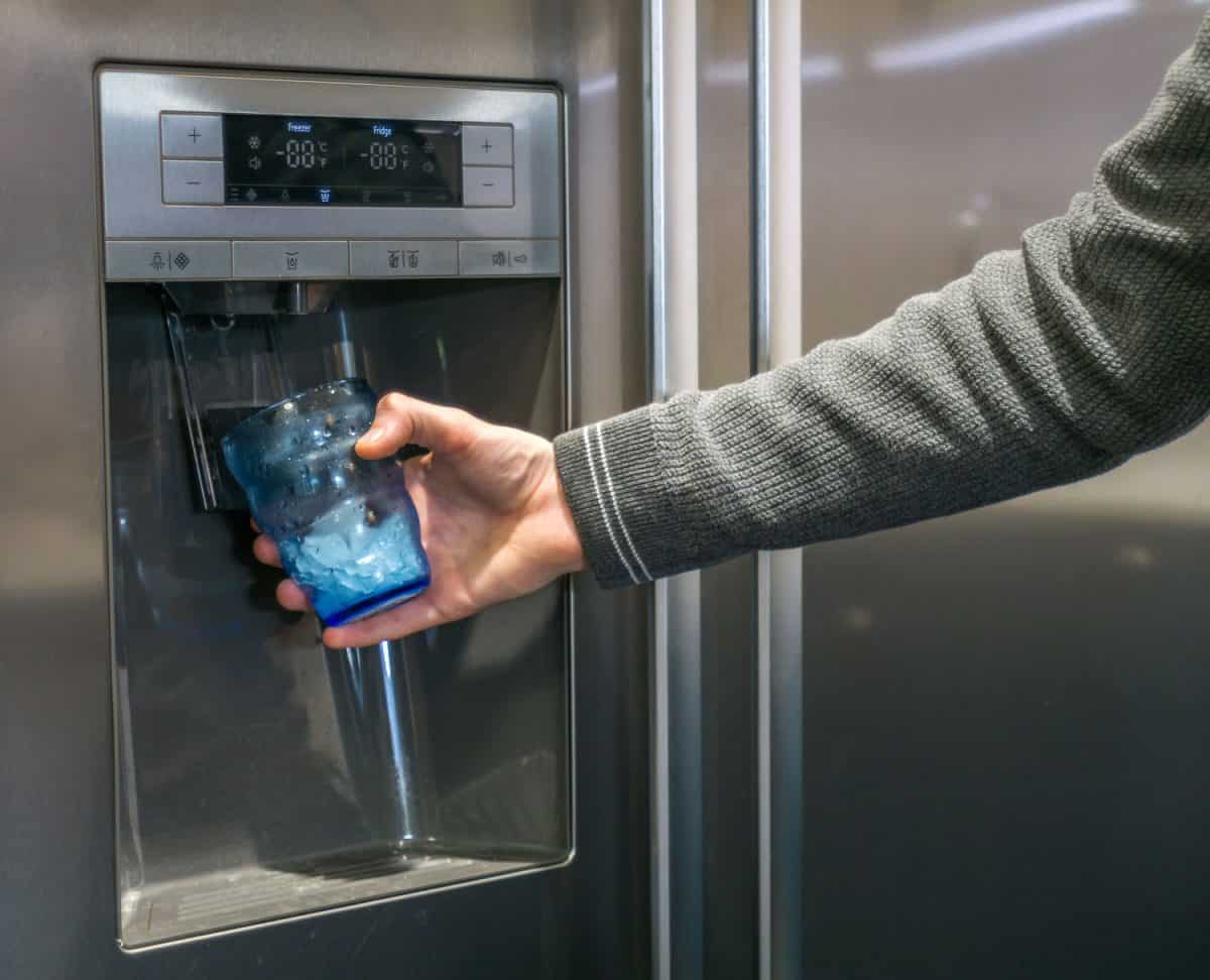 Male-hand-is-pouring-cold-water-and-ice-cubes-from-dispenser-of-home-fridge