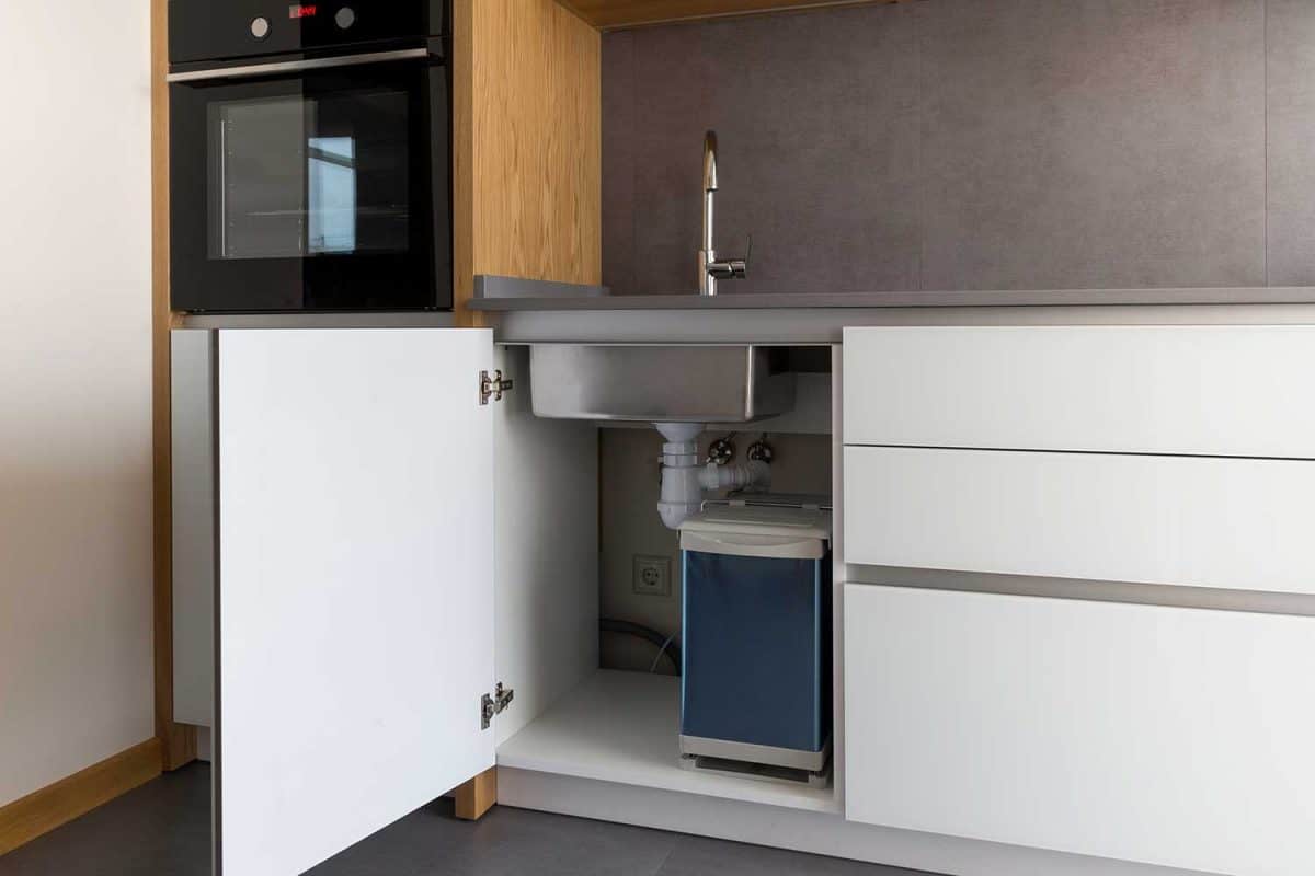 Opened kitchen cabinet with sink and installed garbage bin