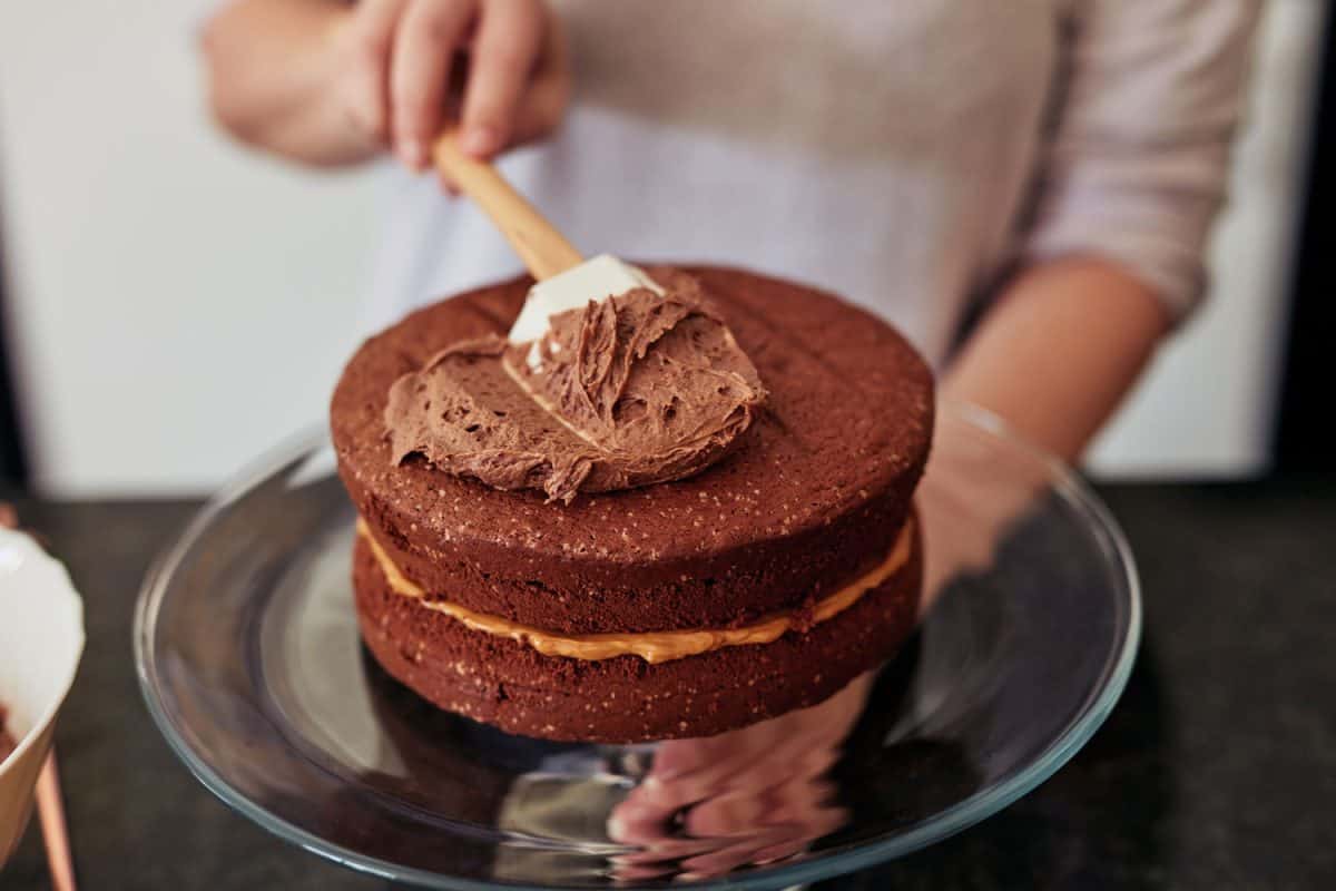 Shot of an unrecognisable woman spreading buttercream on a freshly baked chocolate cake at home